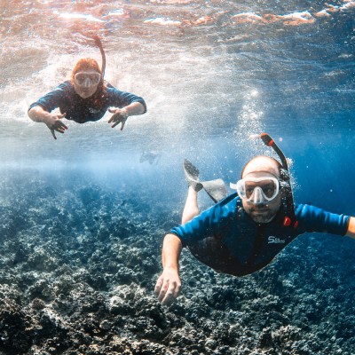 Two snorkelers underwater above a coral reef in clear blue water.
