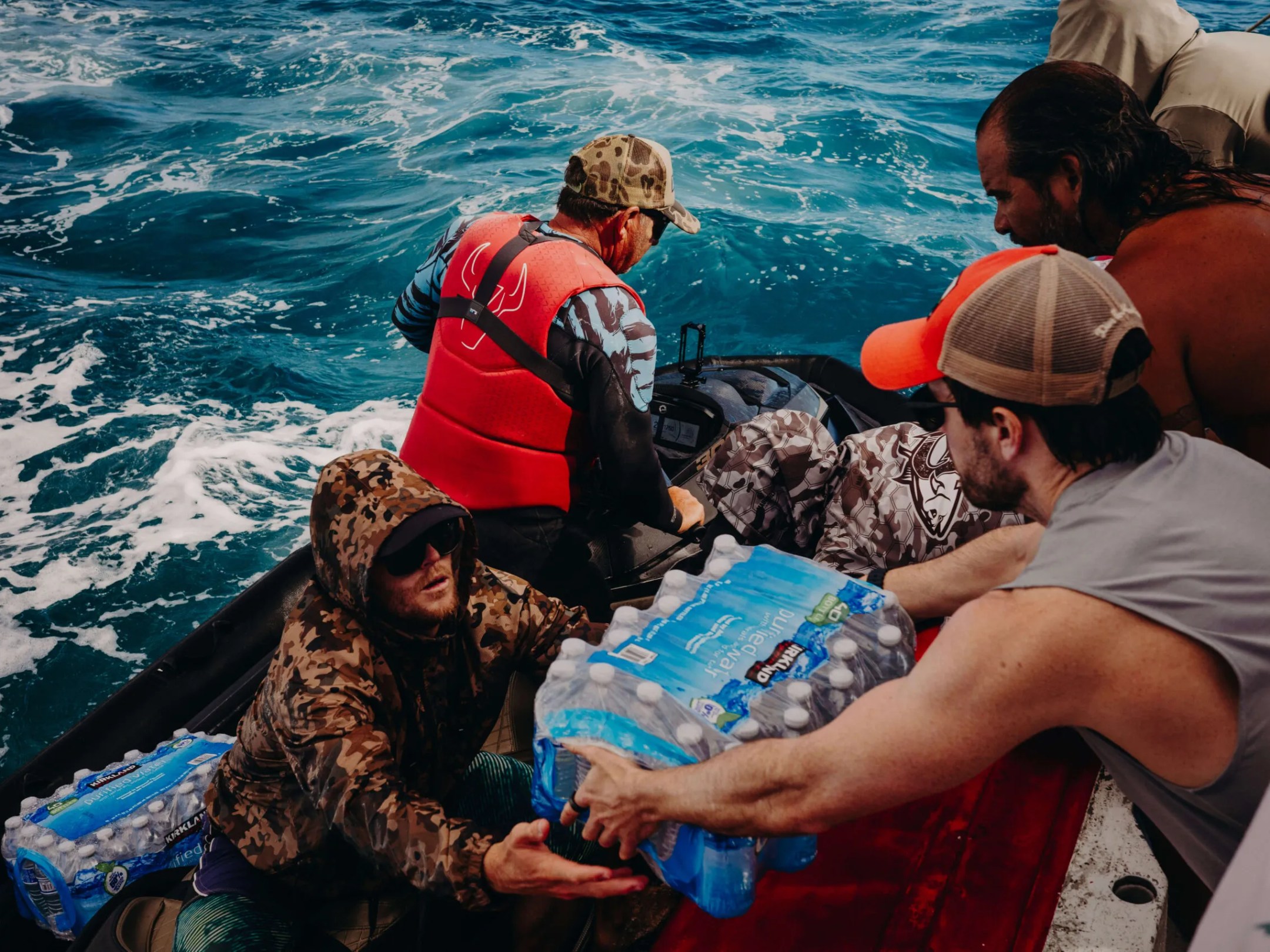 People transfer bottled water between boats on rough sea.