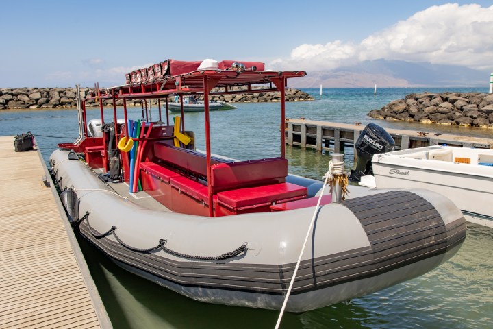 Inflatable boat with red seating and equipment docked by a wooden pier, with hills in the background.
