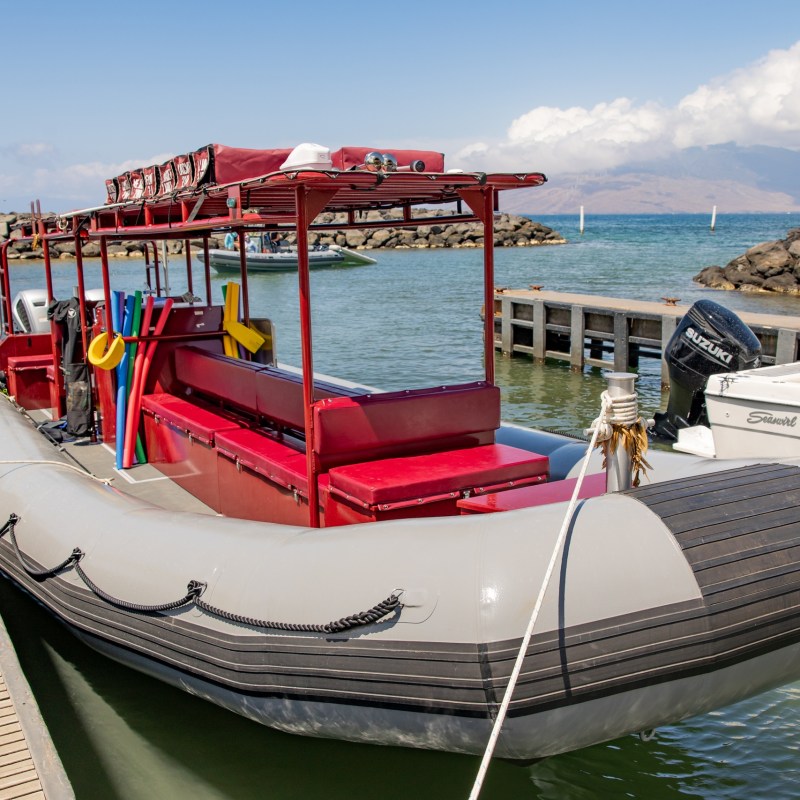 Inflatable boat with red seating and equipment docked by a wooden pier, with hills in the background.