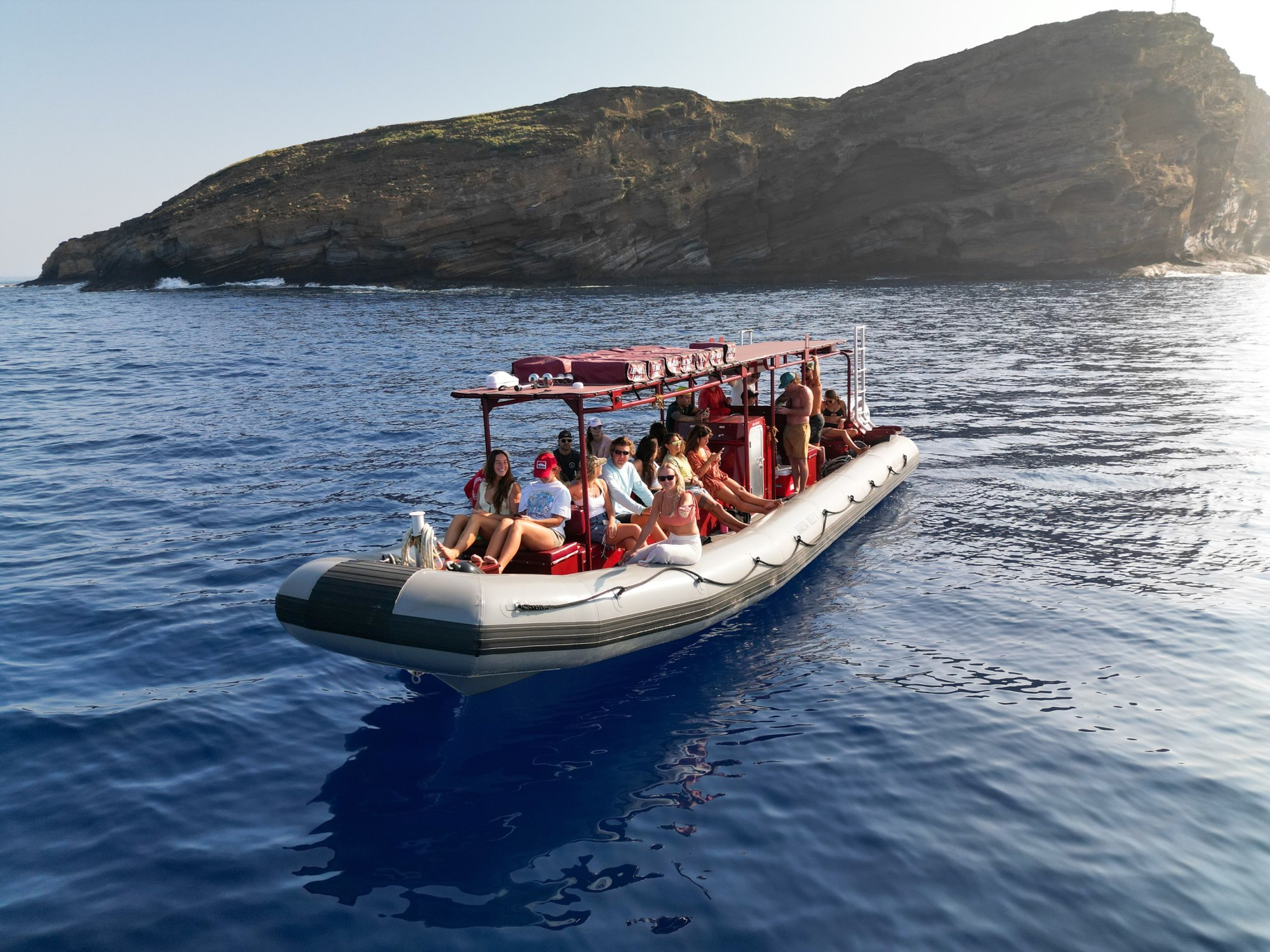 People on a small inflatable boat near a rocky island in clear blue water.