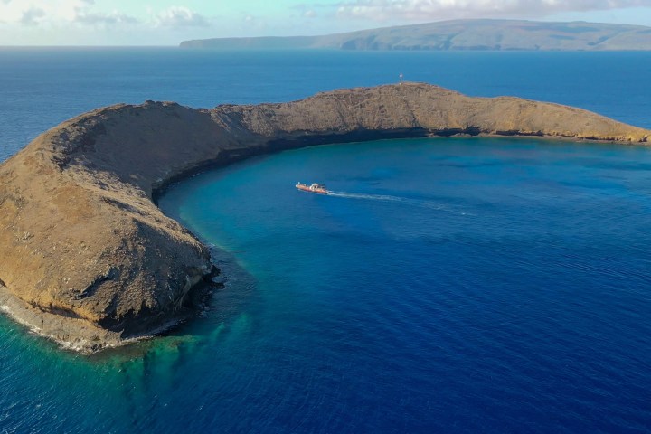 Aerial view of a crescent-shaped island surrounded by blue ocean and a boat in the water.