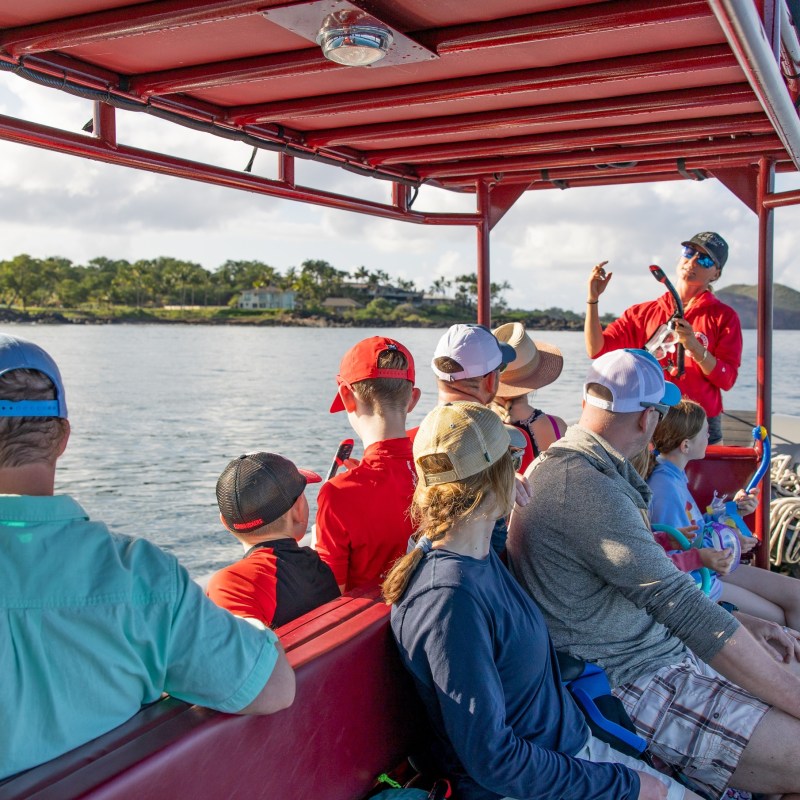 People on a boat with a guide speaking, surrounded by water and distant green landscape.
