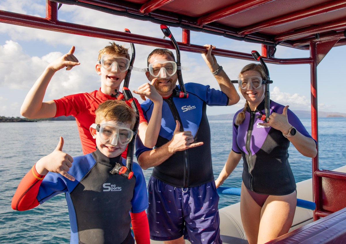 Family in snorkeling gear making hand signs on a boat.