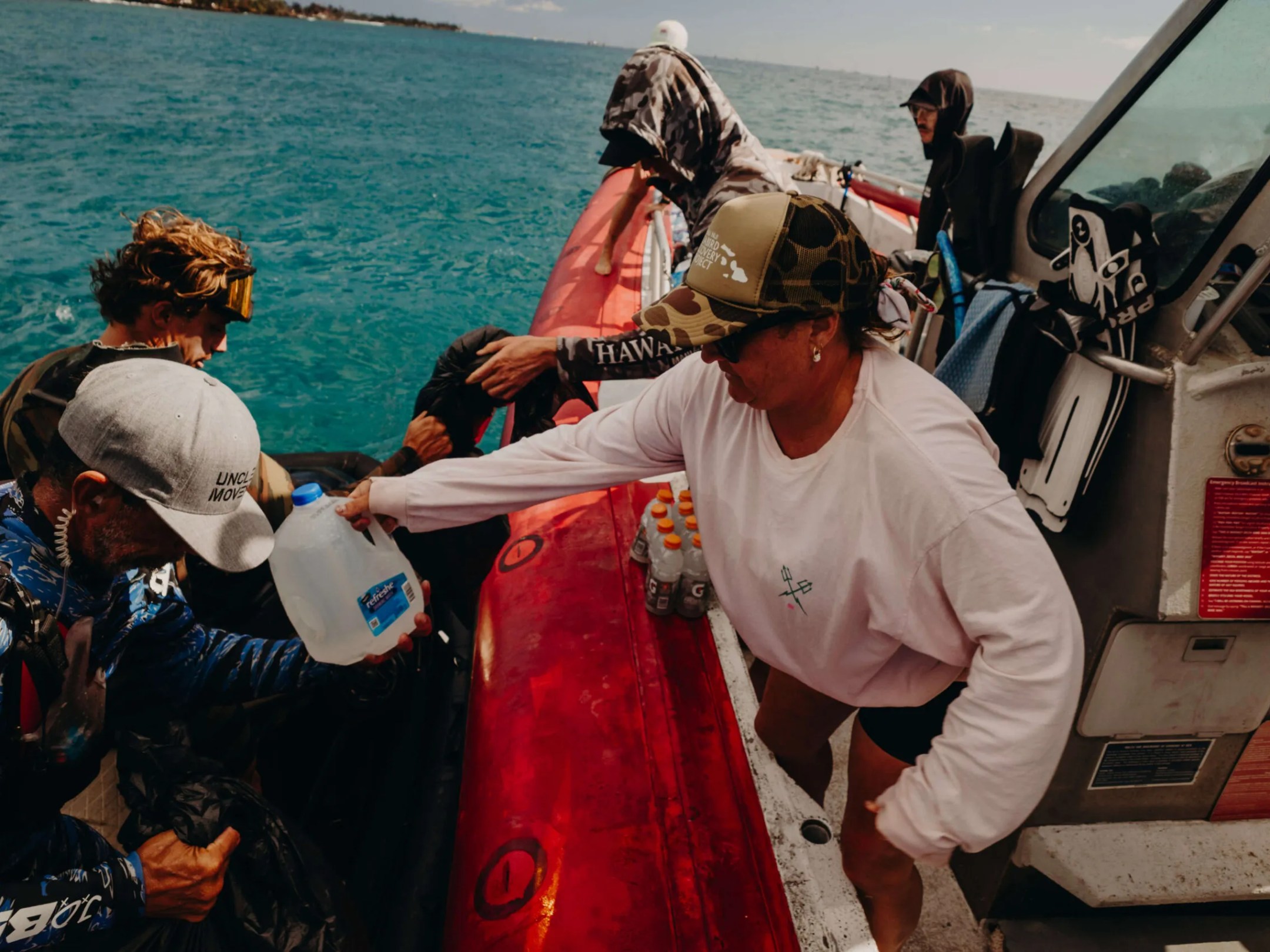 People on a boat passing a jug of water to another vessel on the ocean.