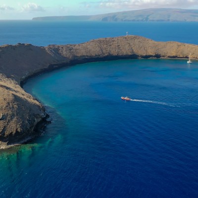 Aerial view of crescent-shaped island in blue ocean with boats nearby.
