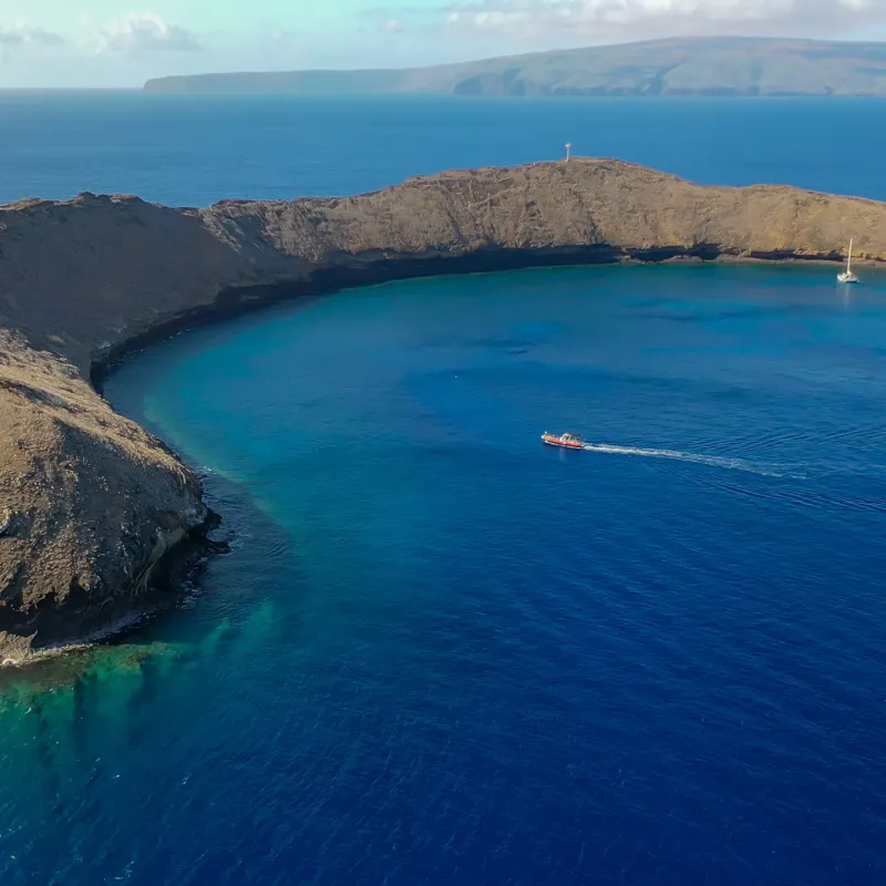 Aerial view of crescent-shaped island in blue ocean with boats nearby.