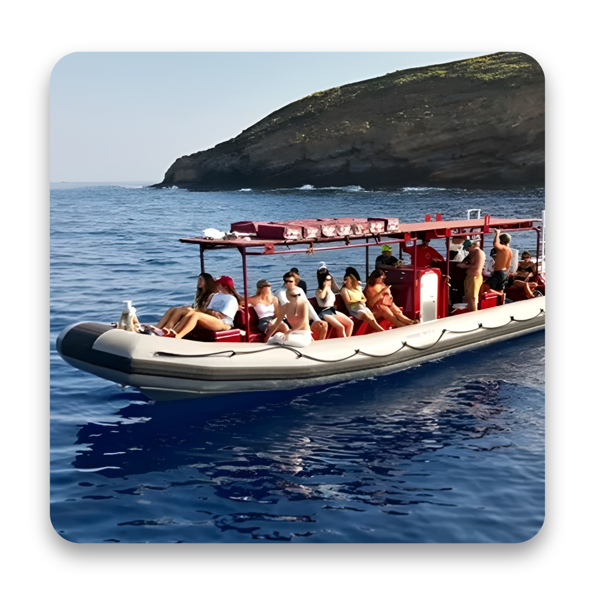 Group of people on a red and white boat in calm blue waters near a rocky island.