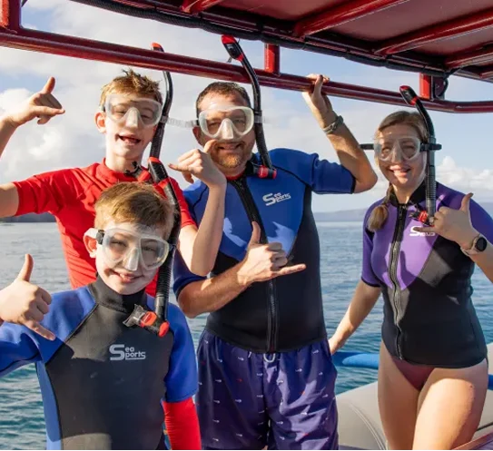 Four people in snorkeling gear posing on a boat, making hand gestures.