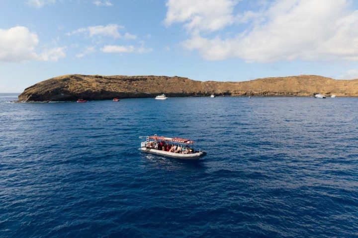 Boat on ocean near small, rocky island under cloudy sky.