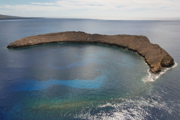 Aerial view of a crescent-shaped island surrounded by blue ocean.