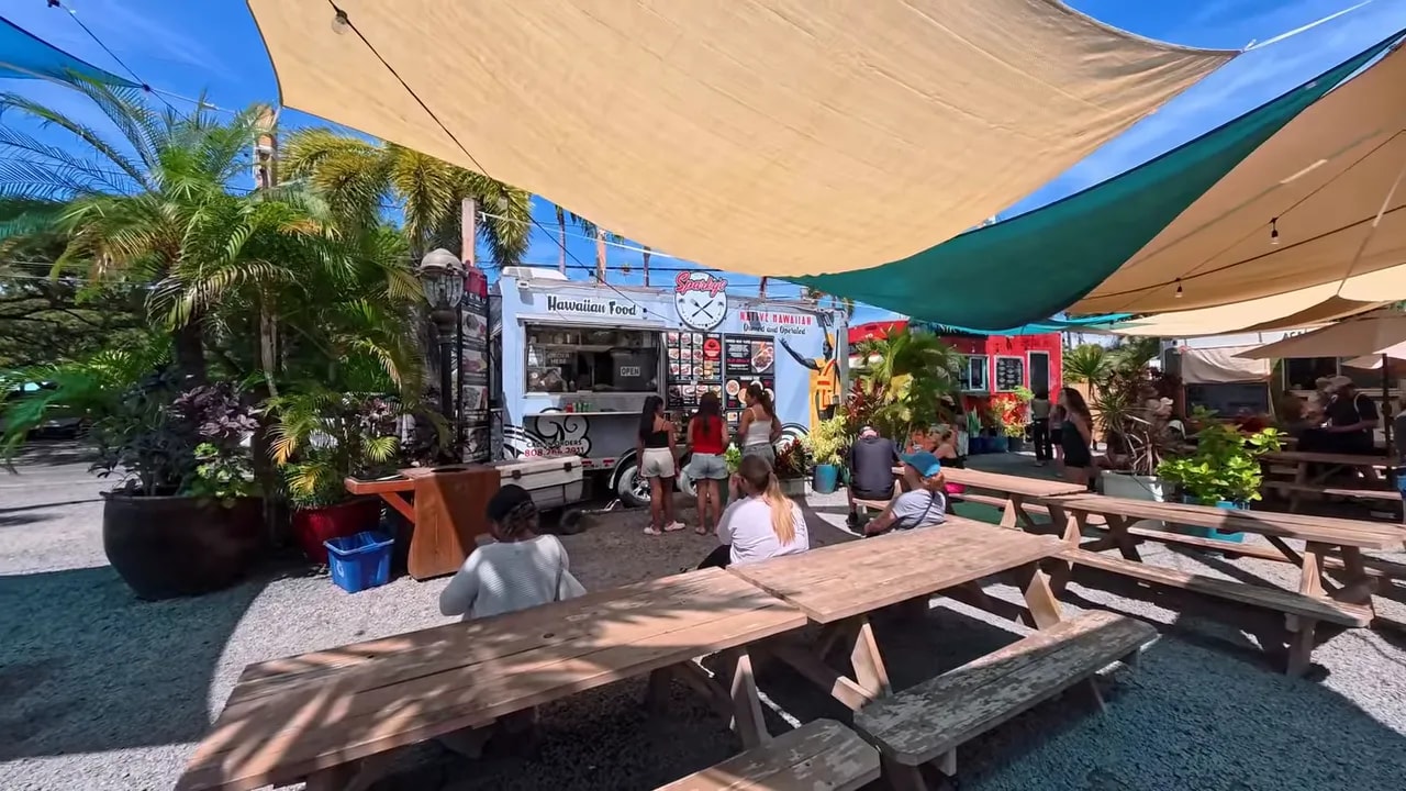 Picnic tables and food trucks beneath colorful shade sails at South Maui Gardens